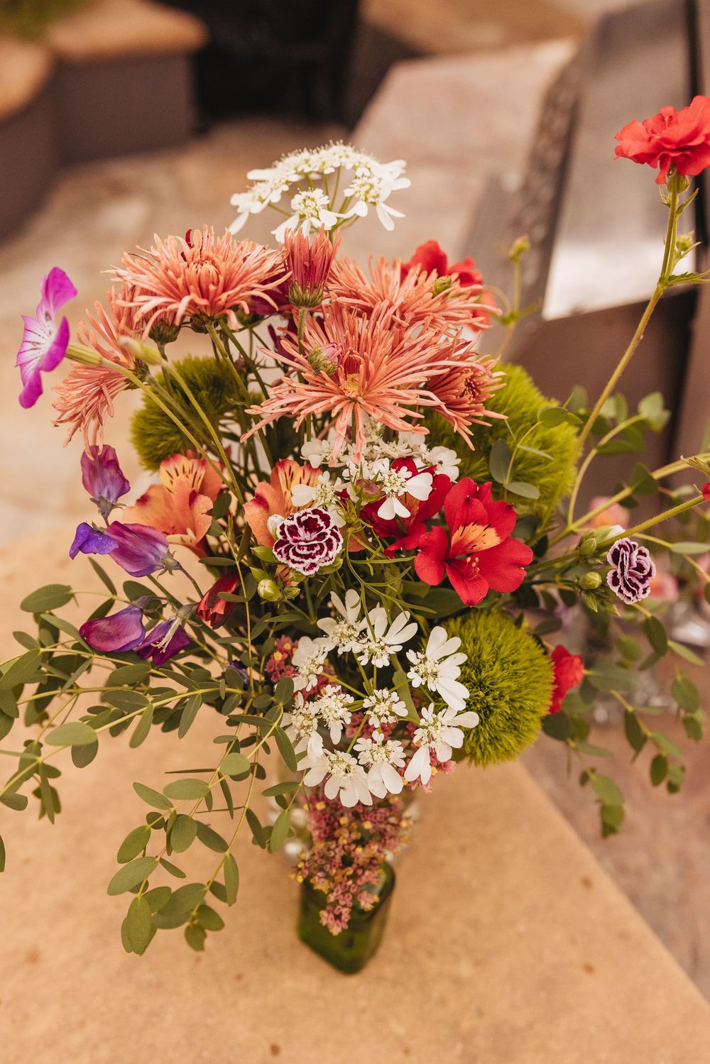 Colorful mixed flower bouquet with pink chrysanthemums, red blooms, white wildflowers, and purple flowers in a glass vase.