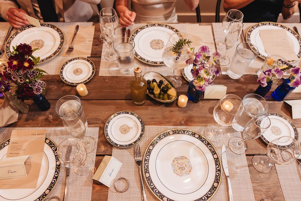 Elegant table setting with decorative plates, glassware, candles, and colorful floral arrangements on a rustic wooden table.