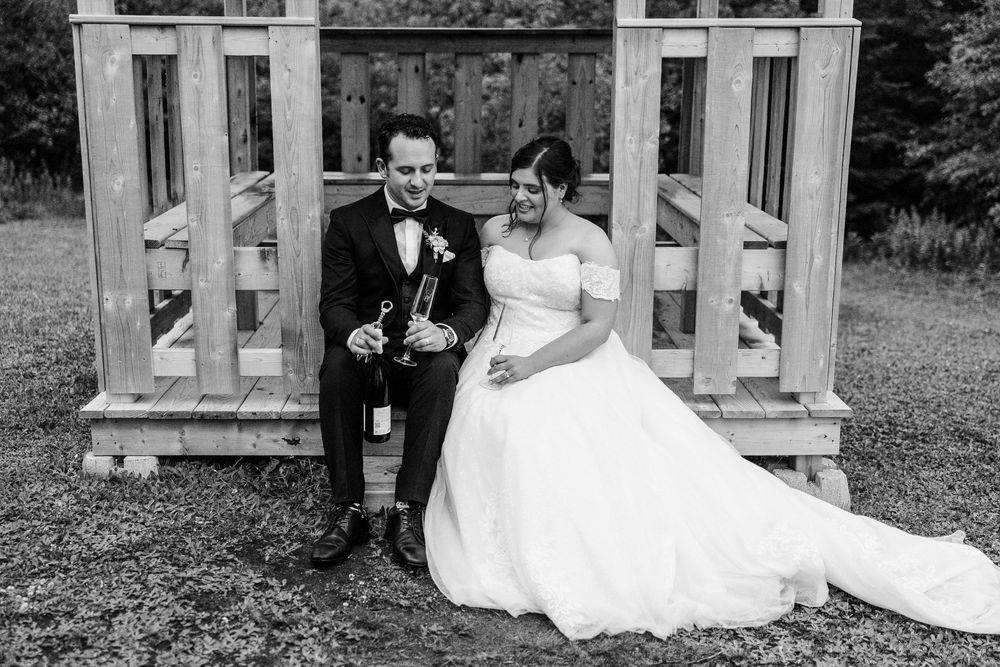 Black and white photo of a bride and groom sitting together outdoors, groom holding a trumpet on their wedding day.
