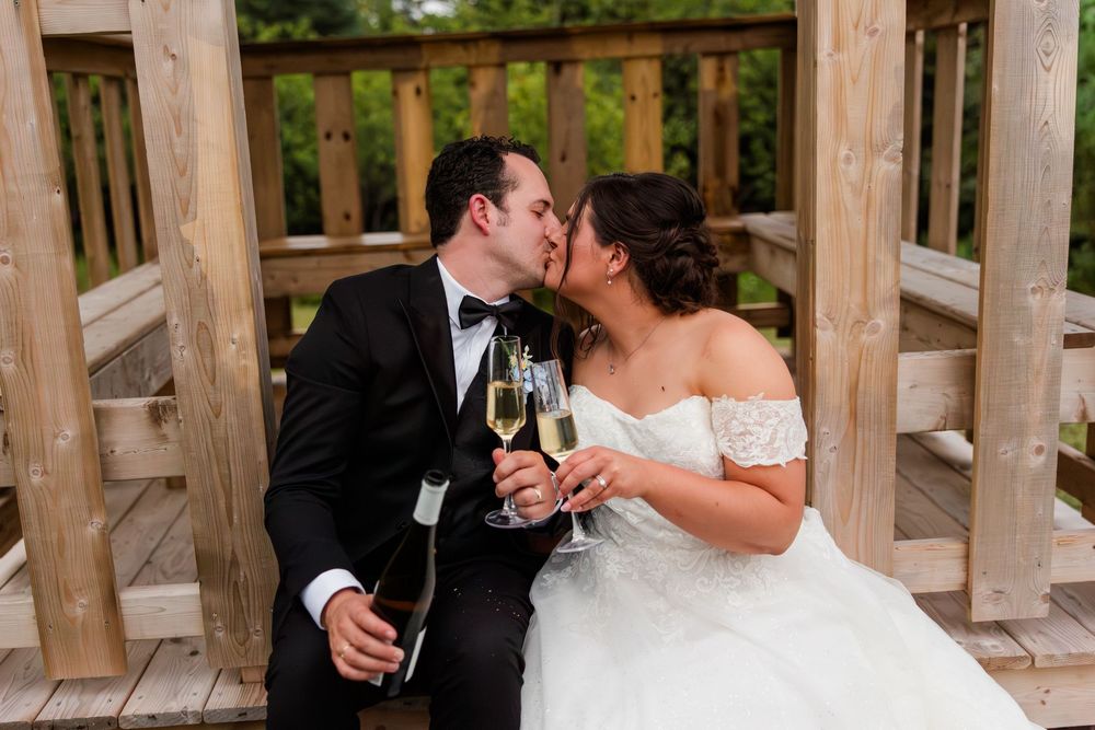 Bride and groom kissing while holding champagne glasses on wooden steps during wedding celebration.