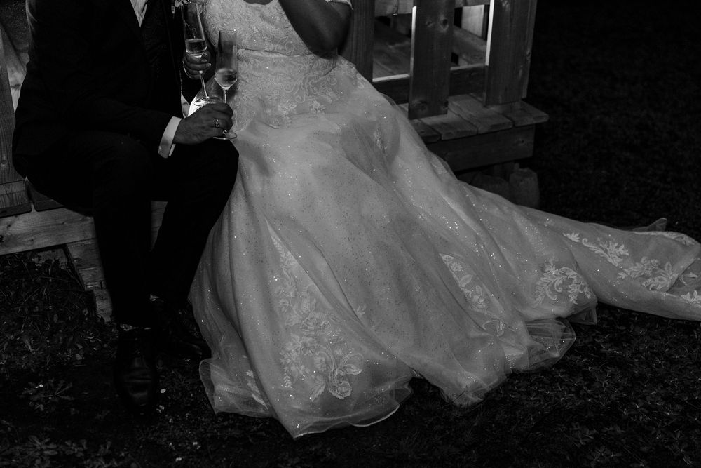 Black and white photo of a bride in a lace wedding gown with a flowing train standing beside a groom in a tuxedo.