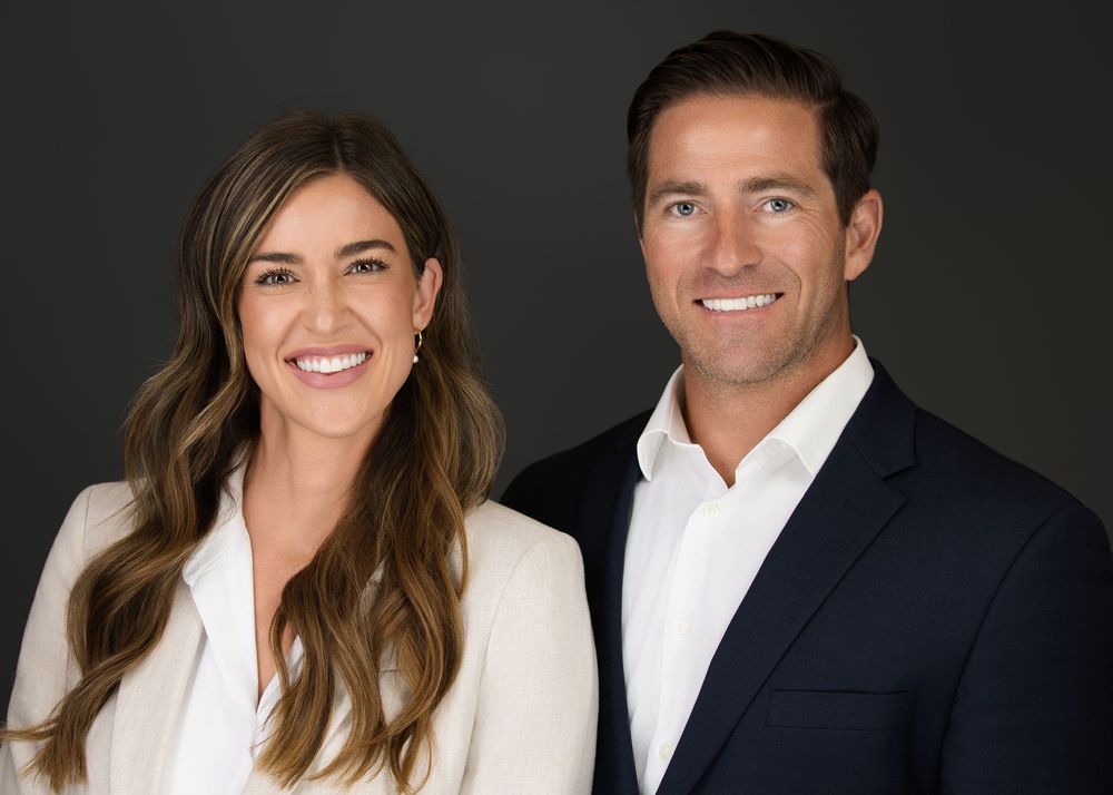 Professional headshot of a smiling man and woman in business attire posed against a dark background.