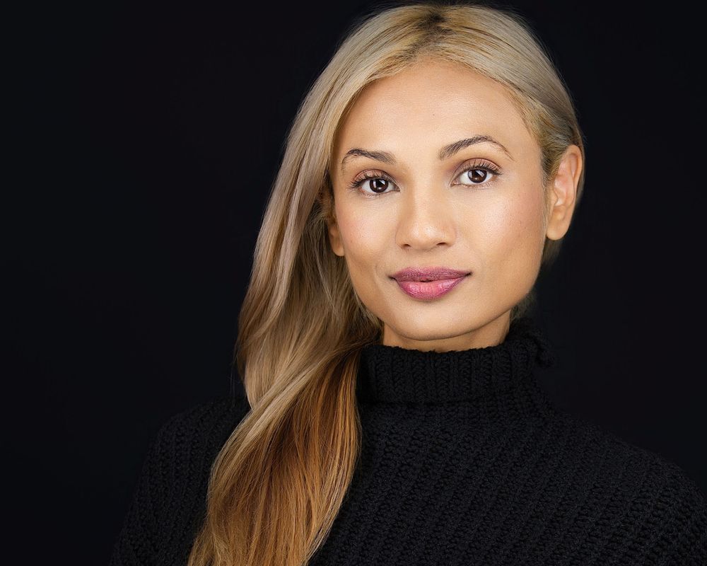 Professional headshot of a young woman with blonde hair wearing a black turtleneck sweater against a dark background.