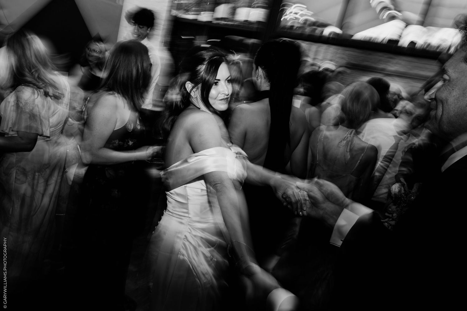 Black and white photo of a bride and groom sharing a romantic moment, bride holding a bouquet, against a white wall.