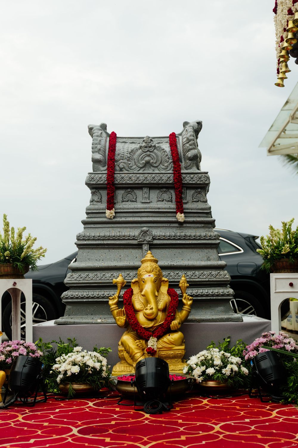 Golden Ganesha idol with red garlands displayed before a stone temple backdrop at a wedding.