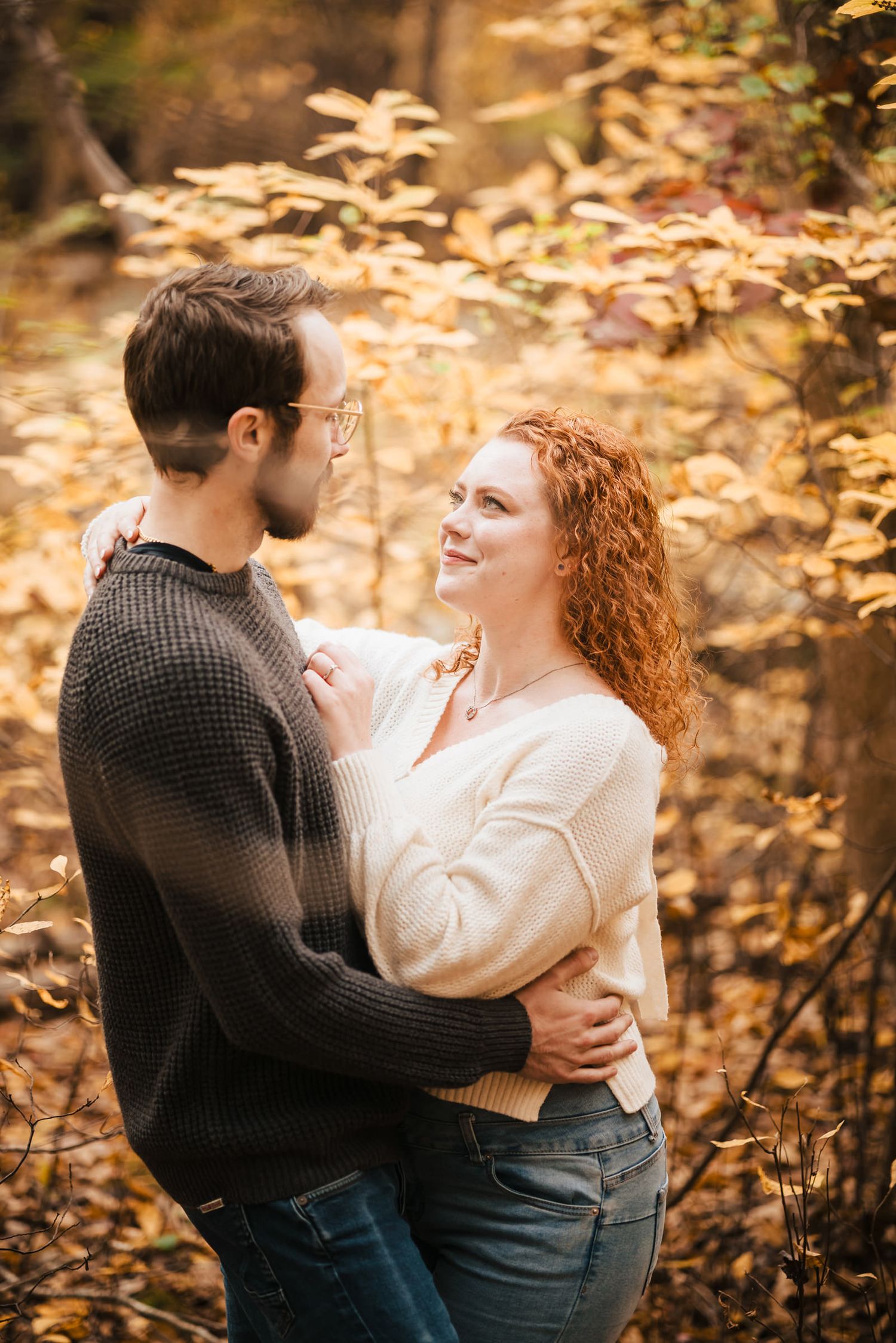 Engaged couple embracing in the forest at Borderland State Park, she looks up at him smiling.