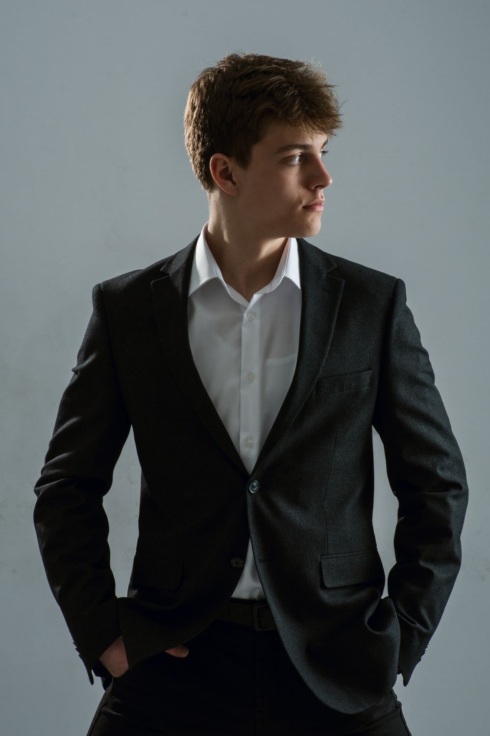 Fashion portrait of model in dark blazer and white shirt against simple gray backdrop.