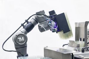 Industrial robotic arm with TM logo holding a brush tool for automated surface finishing tasks.