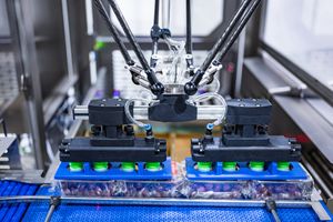 Industrial delta robot arm assembling products on a blue conveyor belt in an automated manufacturing facility.