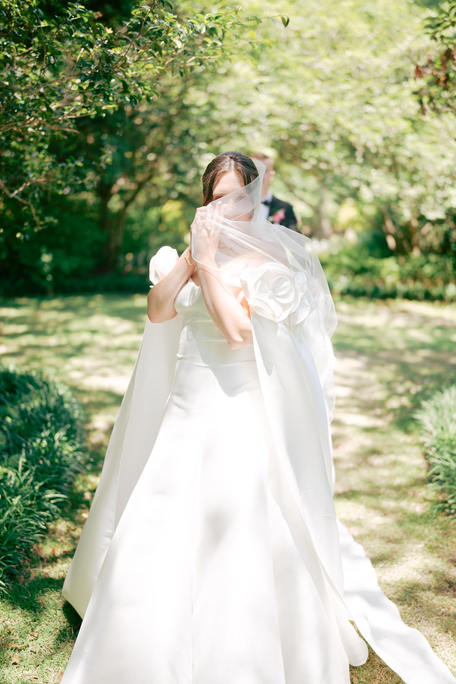 Bride in white ballgown with floral veil blowing in garden.