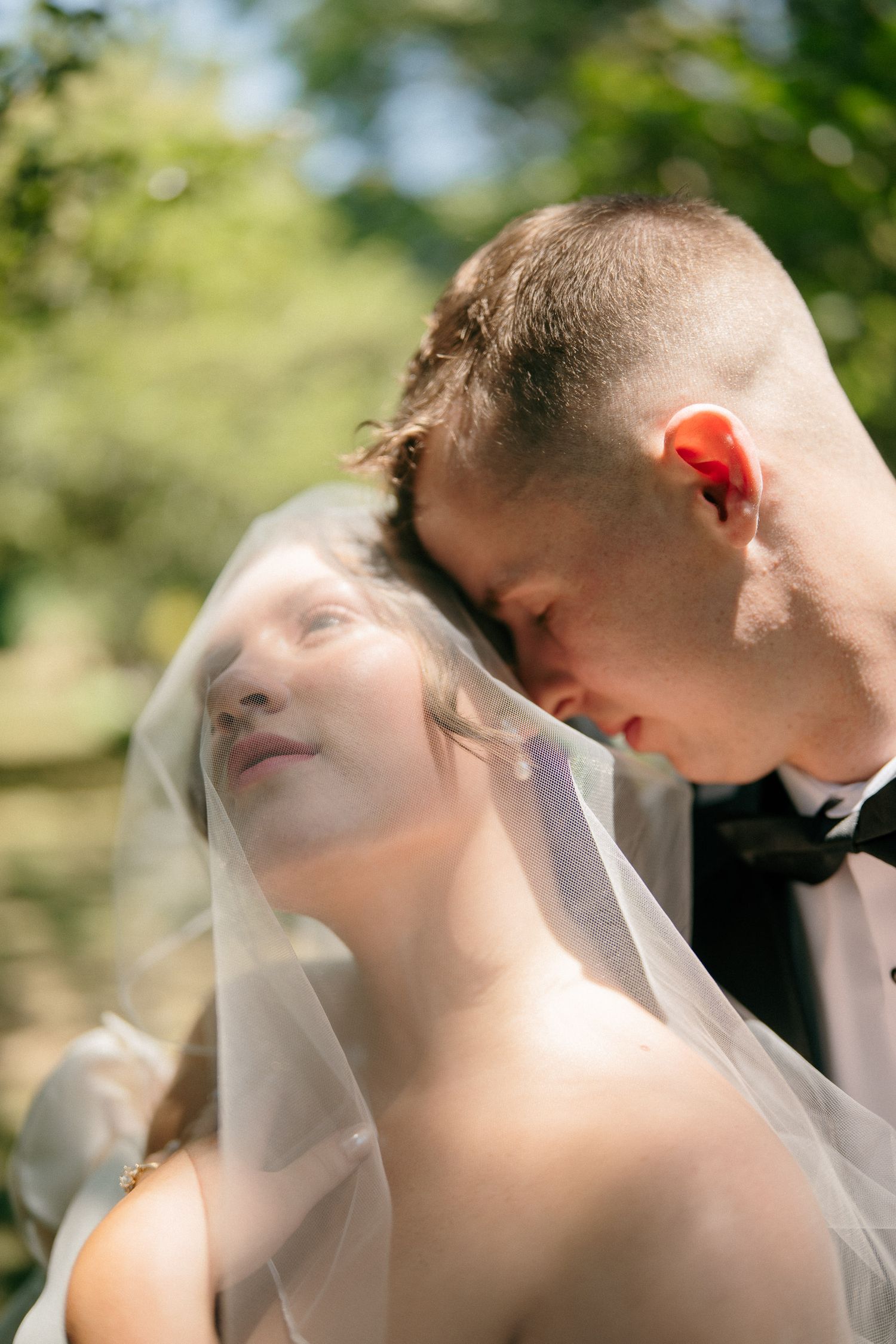 Bride and groom share a tender moment under a veil outdoors on their wedding day.