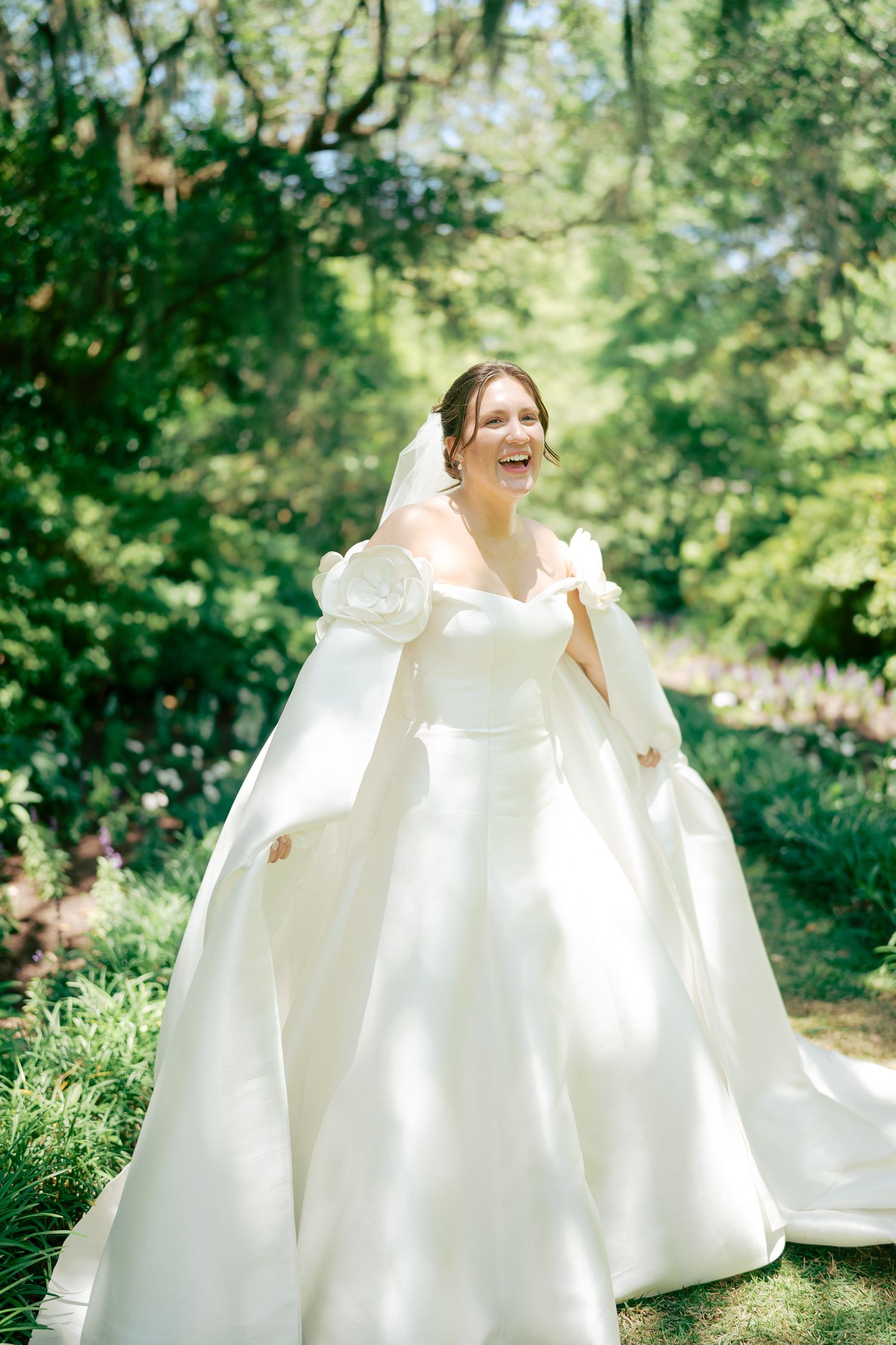 Joyful bride laughing in white ballgown with puff sleeves in sunny garden.