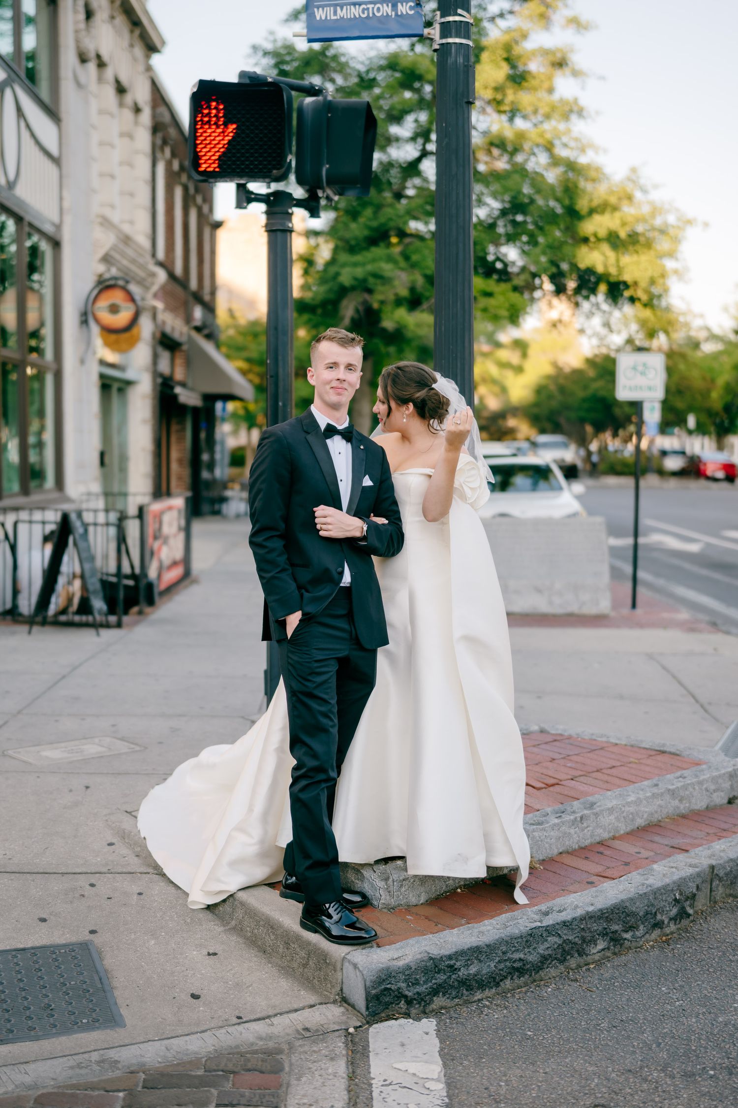 Bride and groom pose at a Wilmington, NC street corner, she in a white gown, he in a black tuxedo.