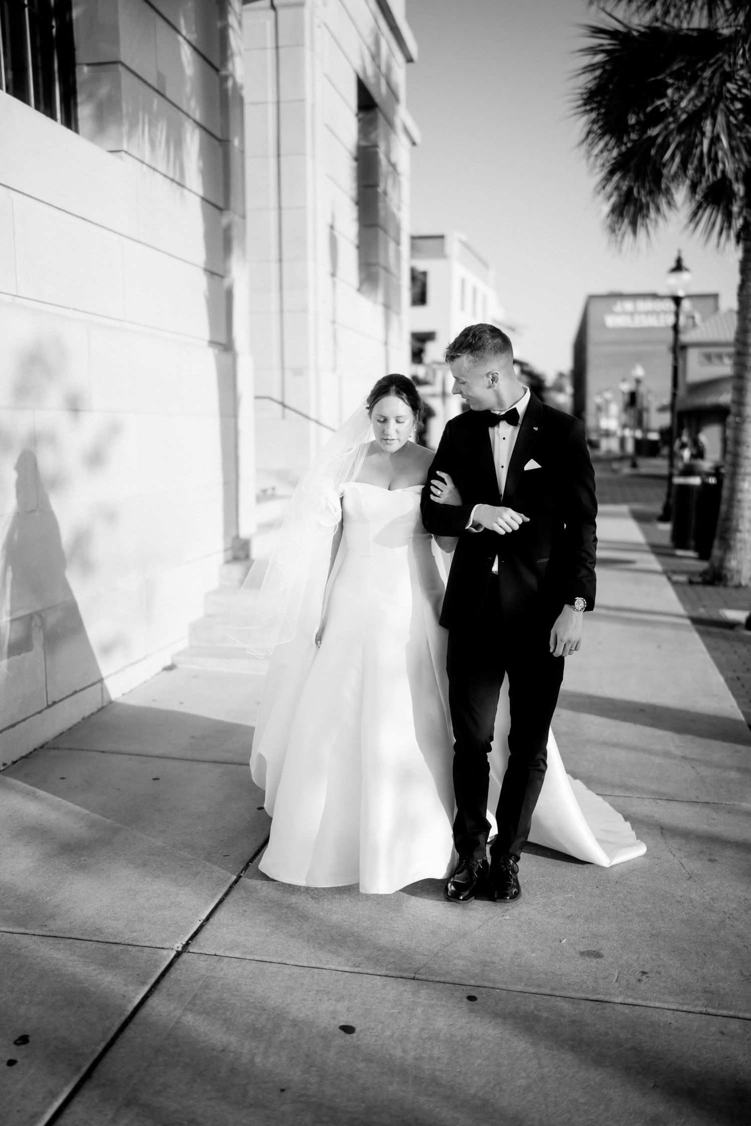 Black and white photo of a bride and groom walking together on a city sidewalk, sharing an intimate moment.