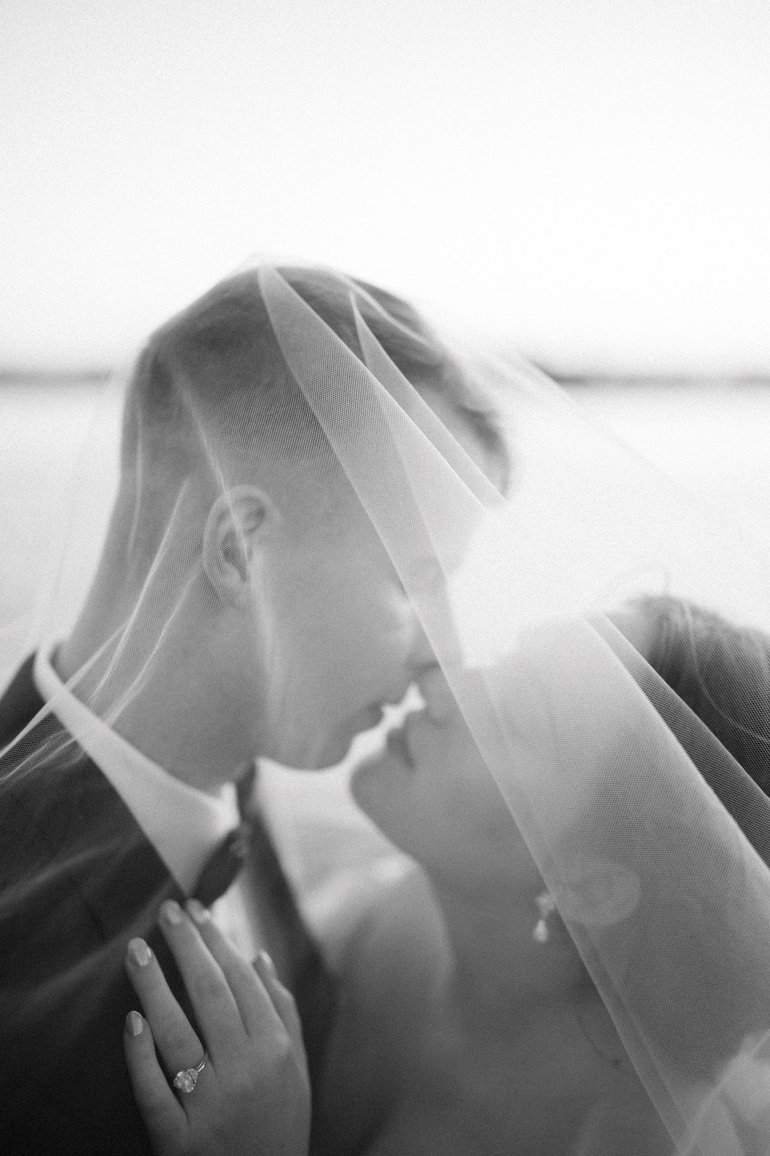 Black and white wedding photo of bride and groom sharing a romantic moment under a veil.