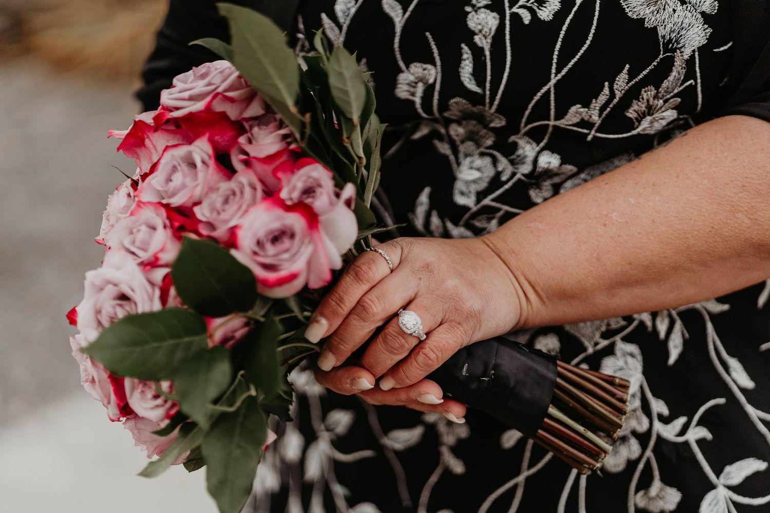 Close-up of a bride holding a pink and red rose bouquet, showcasing a diamond engagement ring on her finger.