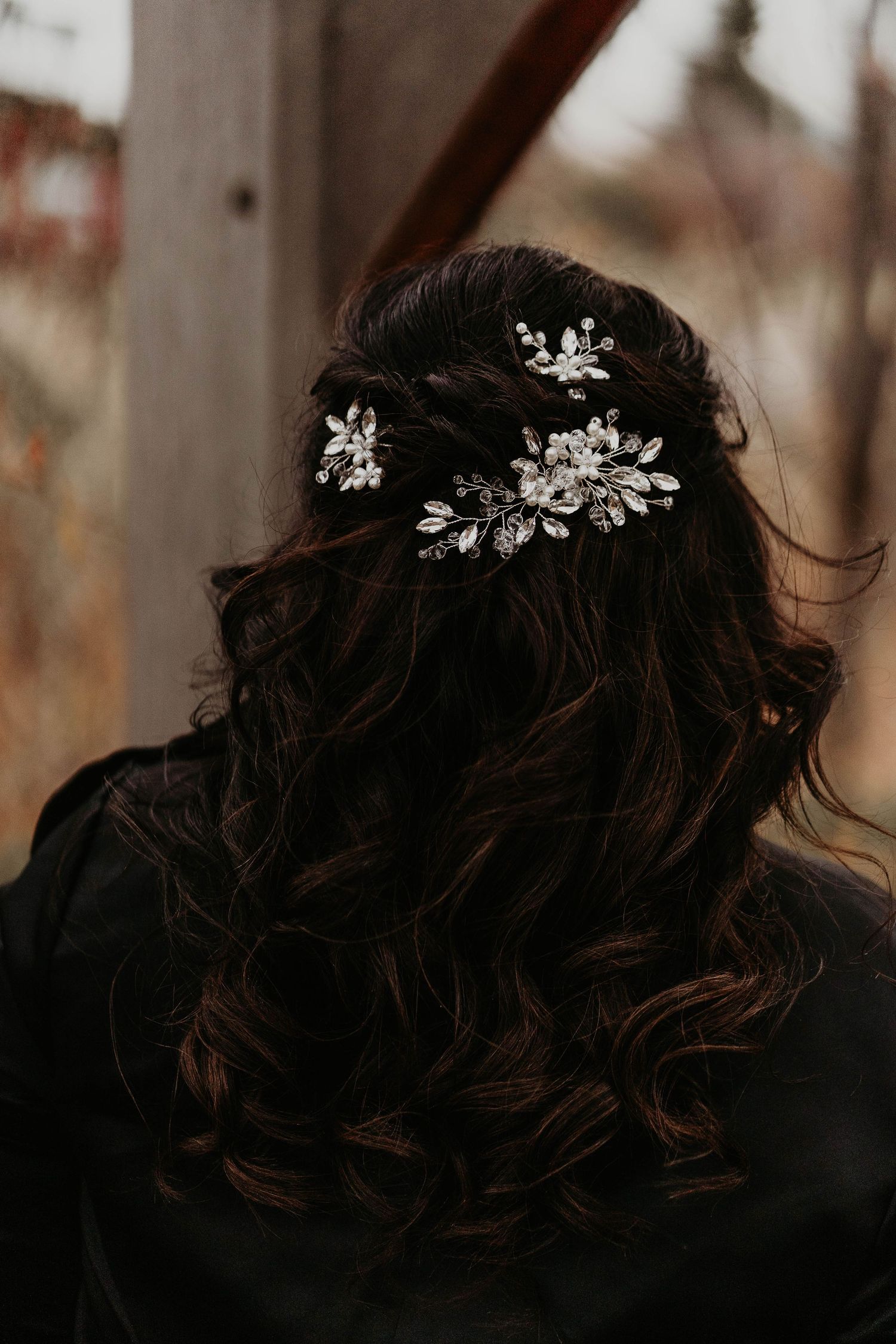 Bride with dark curly hair adorned with silver floral crystal hair pins for a wedding hairstyle.