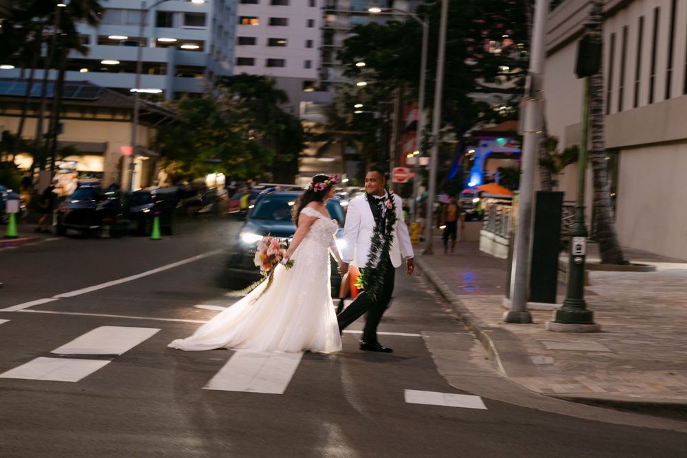 Bride and groom crossing a city street at night, with the bride in a white gown and groom in a suit.