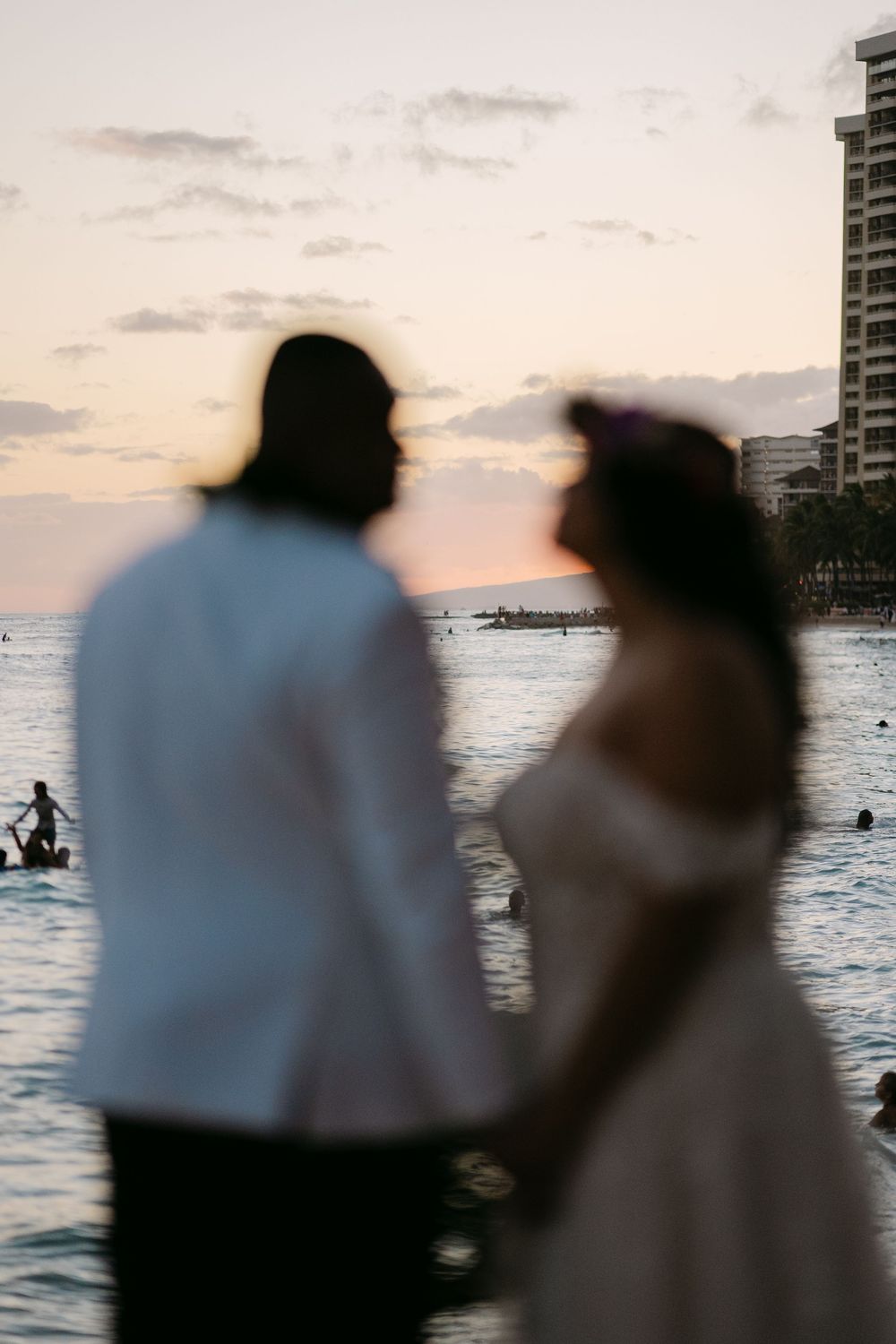 Blurred silhouette of a wedding couple holding hands at sunset on a Hawaiian beach with ocean views.