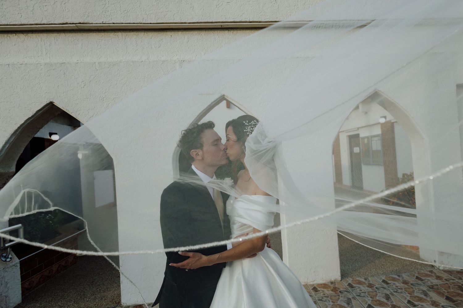 Bride in off-shoulder gown with veil reflected in mirror surrounded by bookshelves.