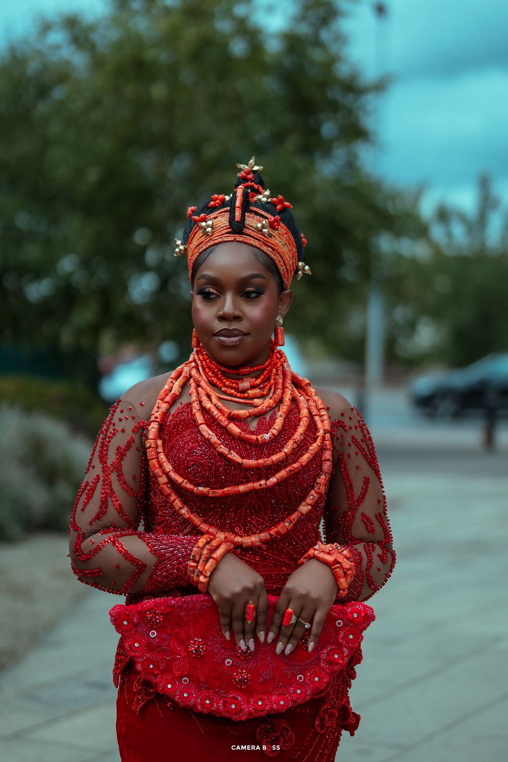 Woman in traditional Nigerian Urhobo red coral beaded bridal attire and headdress poses outdoors.