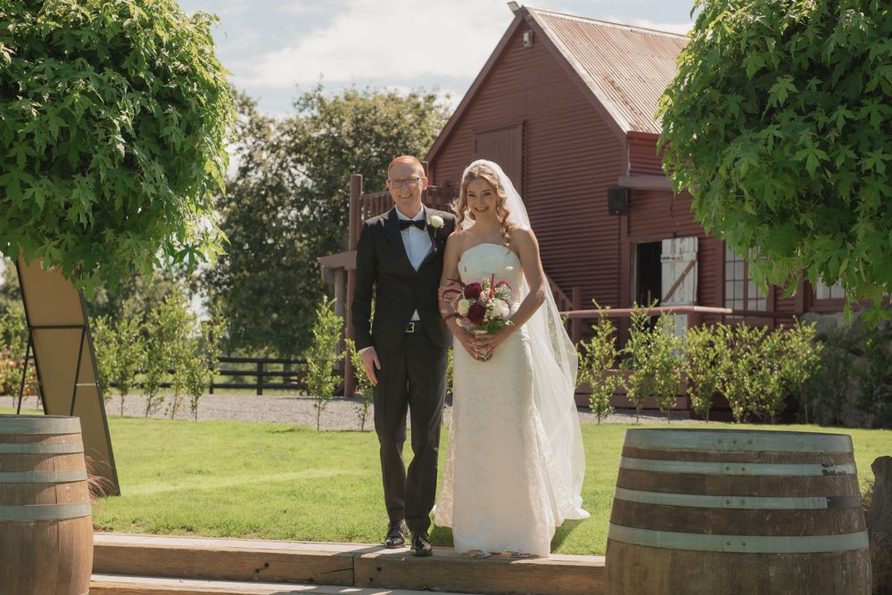 Bride and groom walking together outdoors at a rustic winery wedding venue with wine barrels and red barn.