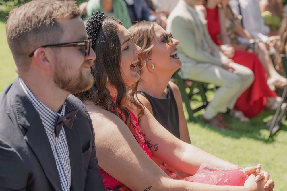 Wedding guests seated outdoors, reacting emotionally during an outdoor ceremony on a sunny day.