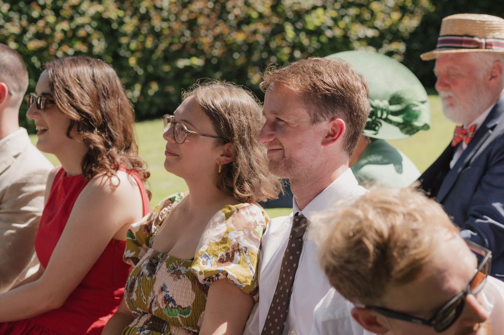 Guests in summer attire enjoying an outdoor garden wedding ceremony on a sunny day.
