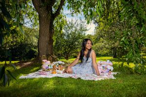 Woman in floral dress enjoying a picnic under a large tree on a sunny day in a lush green park.