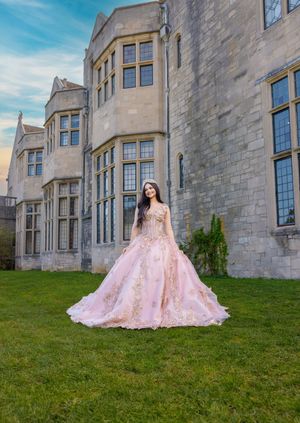 Young woman in pink ballgown poses on castle lawn at dusk.