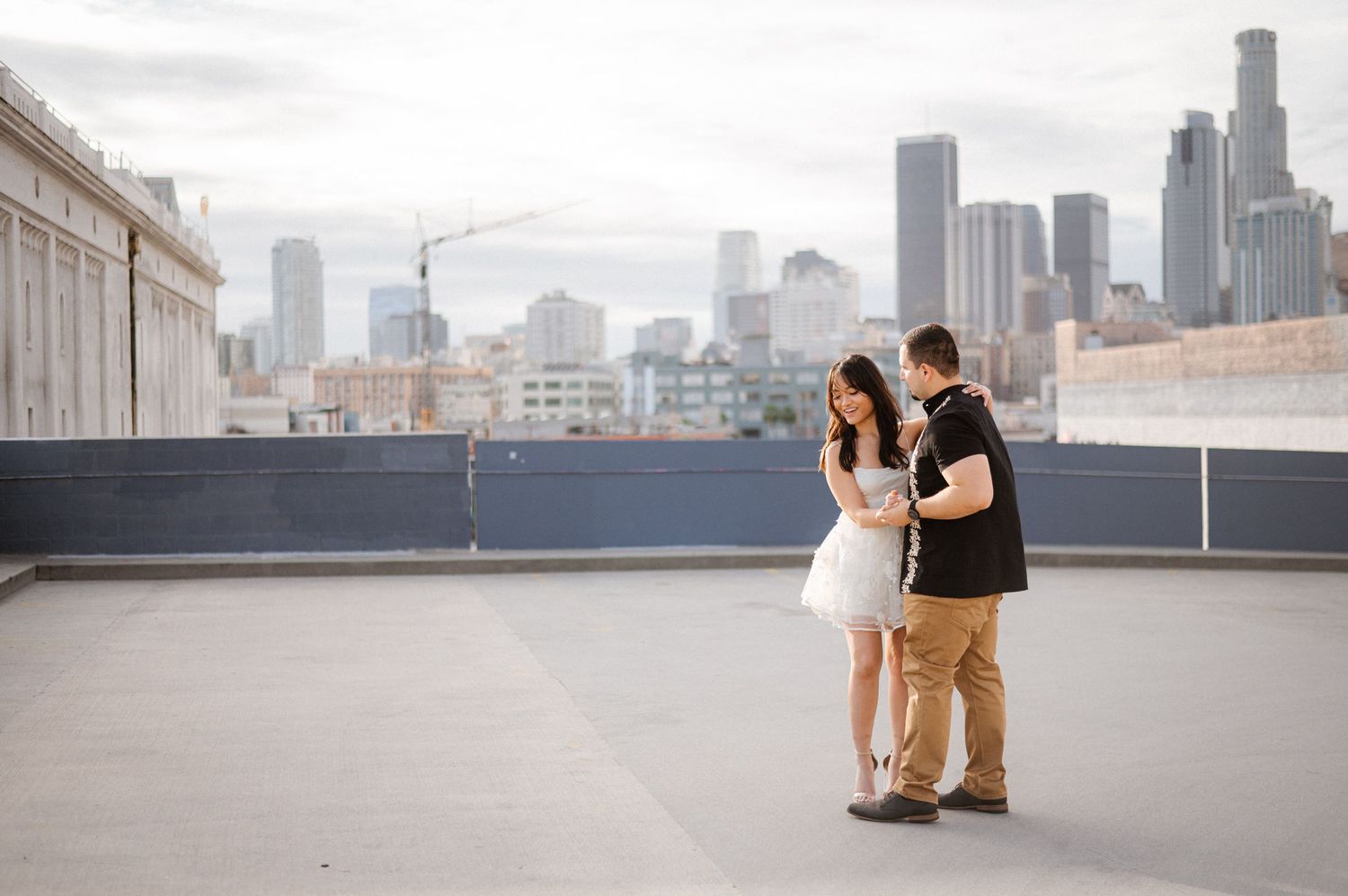 Couple embracing on urban rooftop with downtown skyscrapers in background.