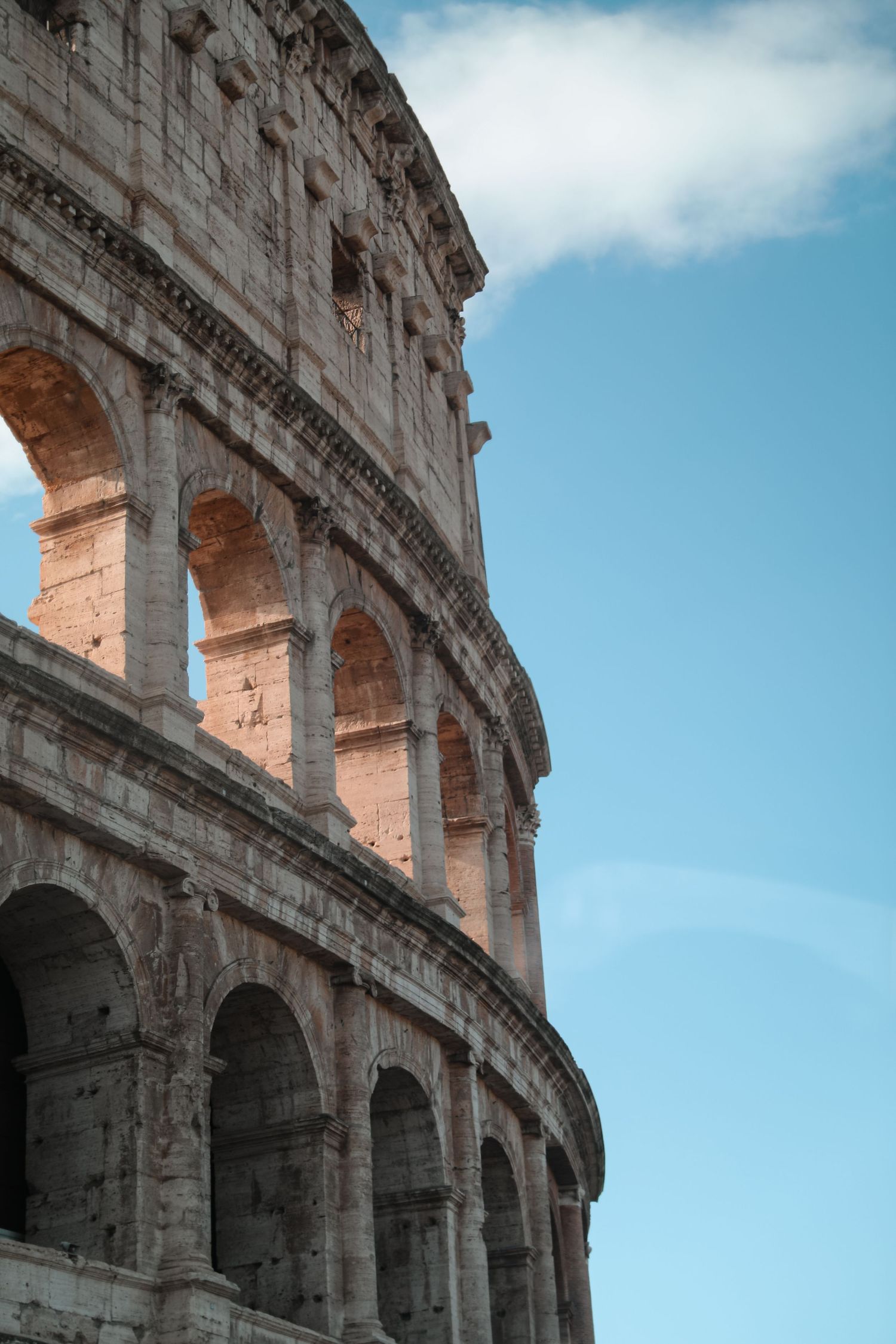 Close-up view of the ancient Roman Colosseum's iconic arched facade against a clear blue sky in Rome, Italy.