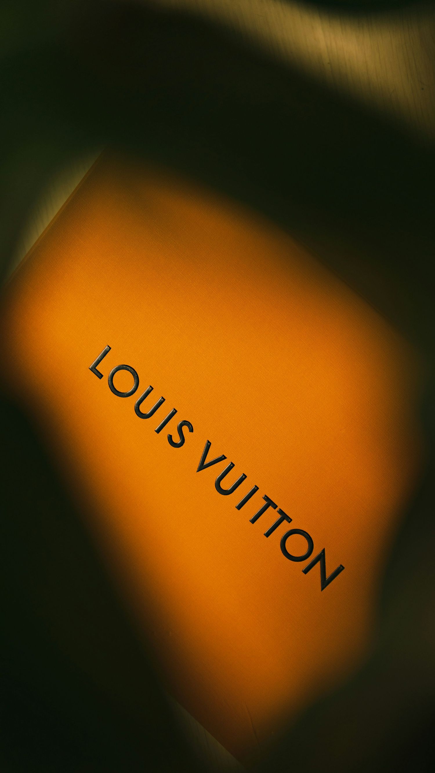 Close-up of Louis Vuitton luxury brand logo on signature orange background with dark dramatic lighting.