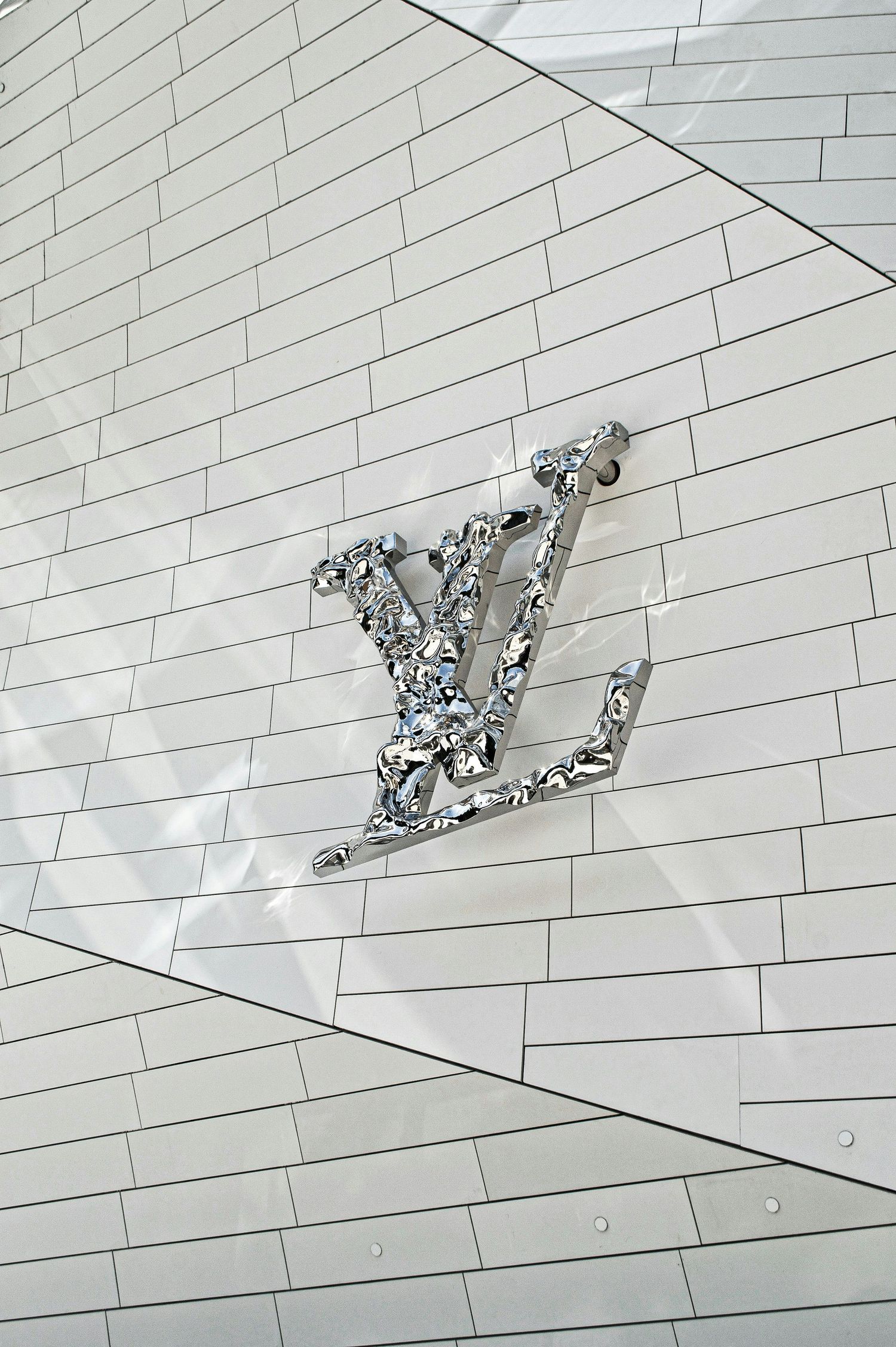 Shiny silver Louis Vuitton LV logo monogram on a white geometric tiled wall facade.