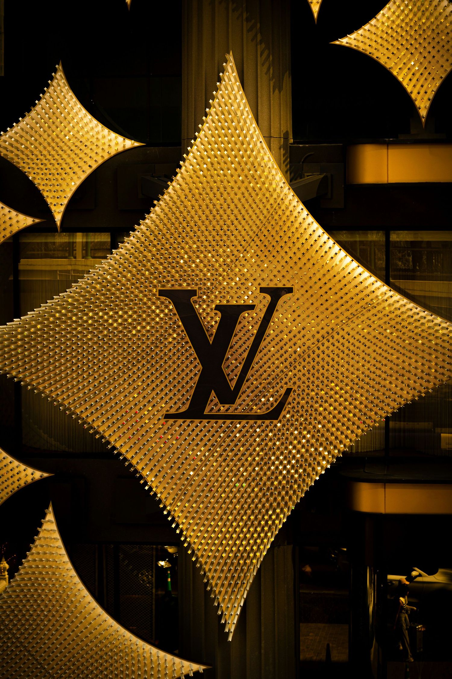 Golden Louis Vuitton LV monogram logo display with glittering diamond-shaped illuminated pattern on luxury store facade.