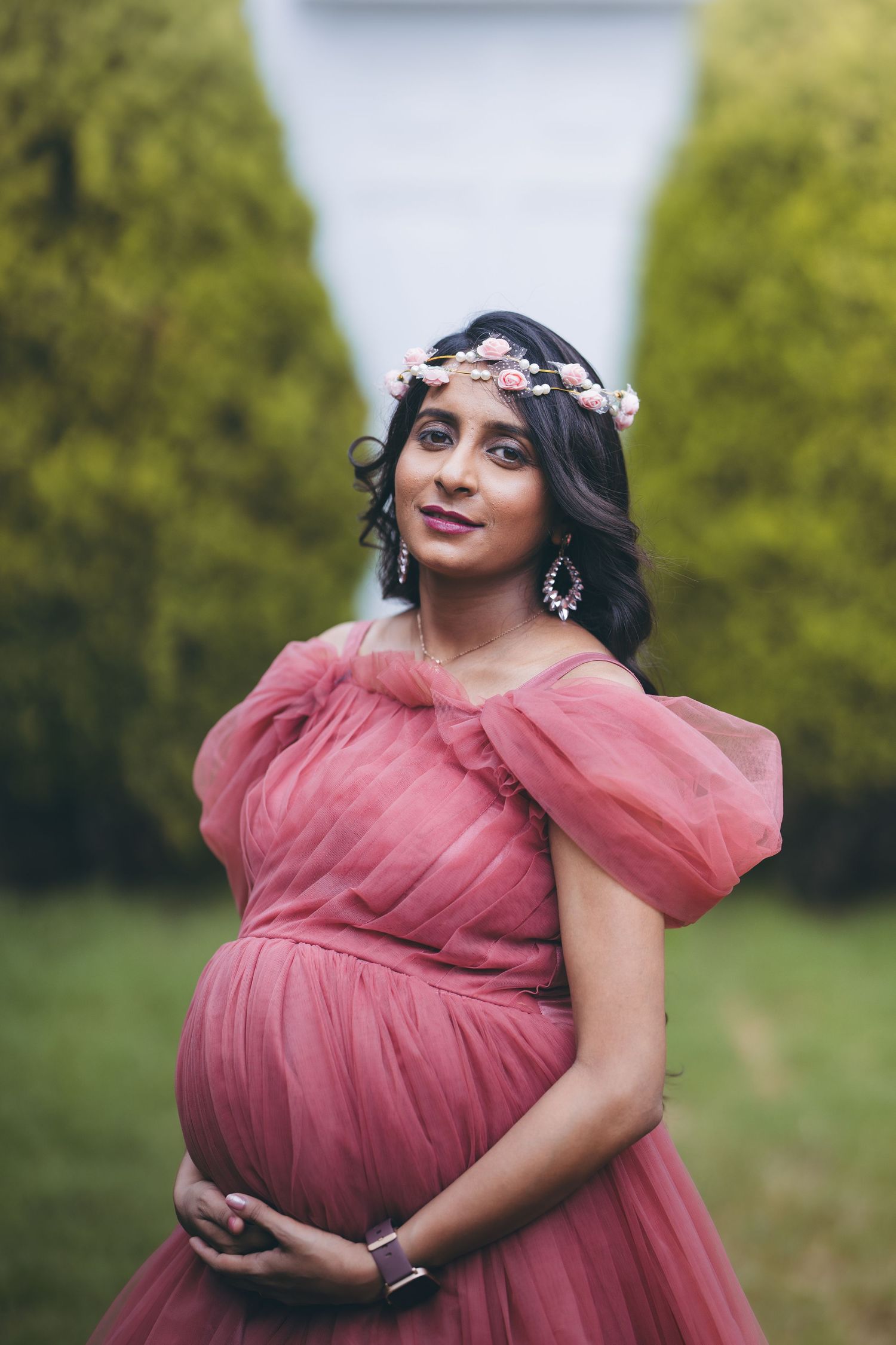 Pregnant woman in black dress posing for maternity photoshoot against white background.