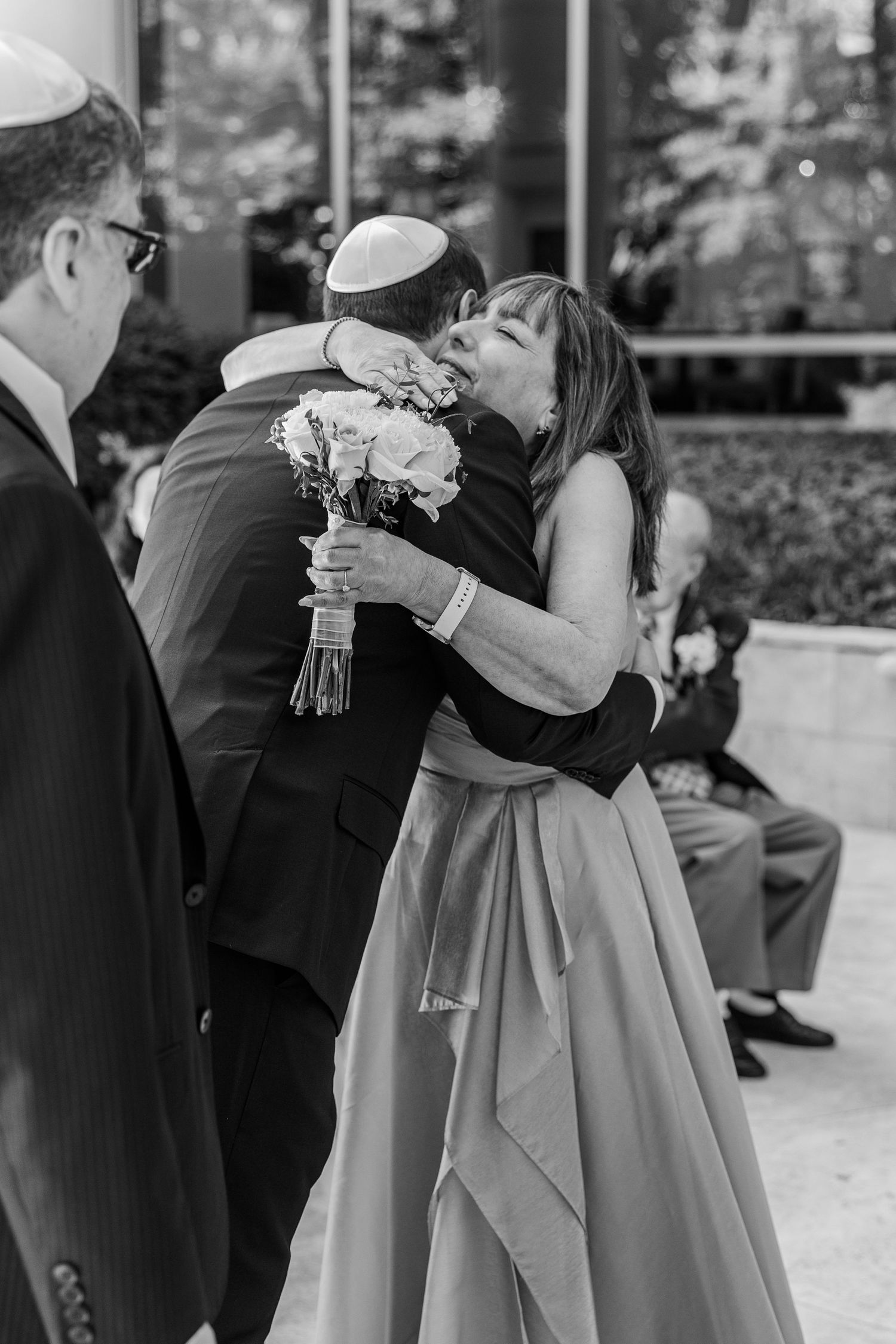 Black and white photo of a woman in a formal gown embracing a man in a suit wearing a kippah at a Jewish wedding.
