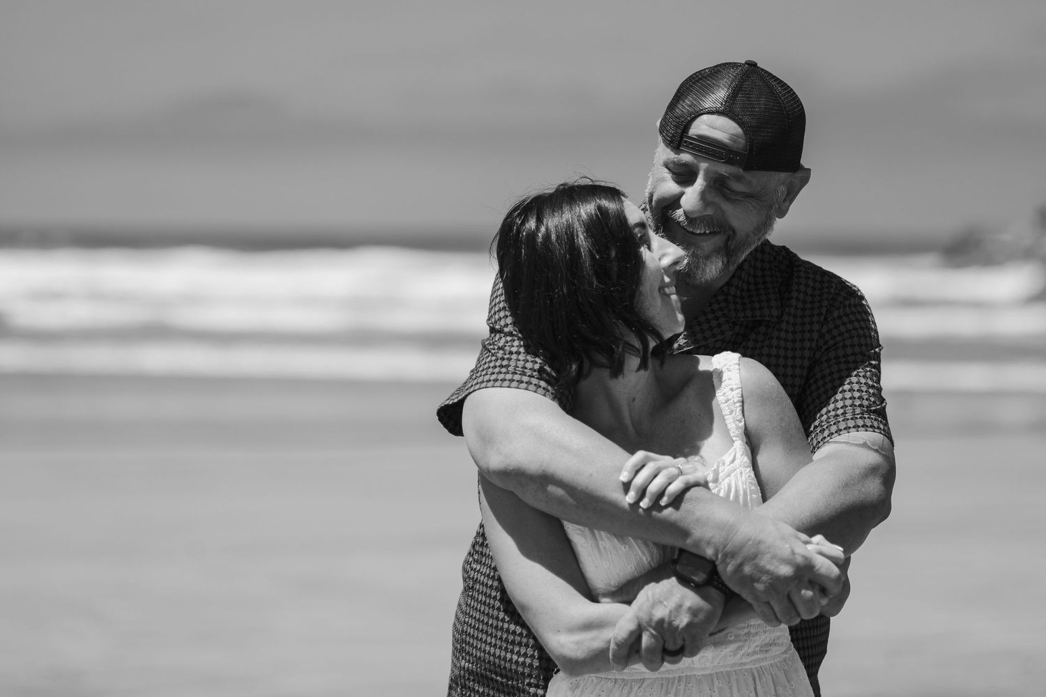 Couple embracing and dancing on a beach in black and white, sharing a romantic moment by the ocean waves. Oceanside, CA
