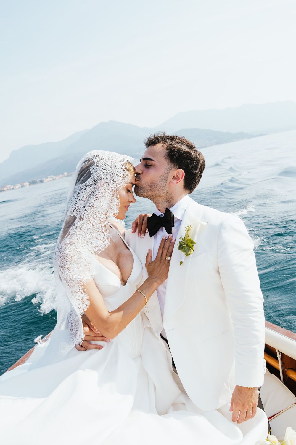 Bride and groom share a kiss on a boat with scenic mountains and blue ocean in the background on their wedding day.