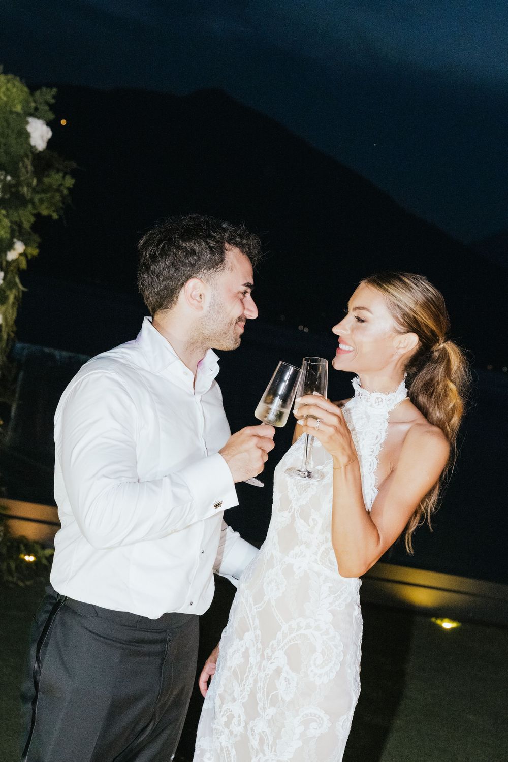 Couple in wedding attire toasting with champagne glasses at night outdoor celebration.