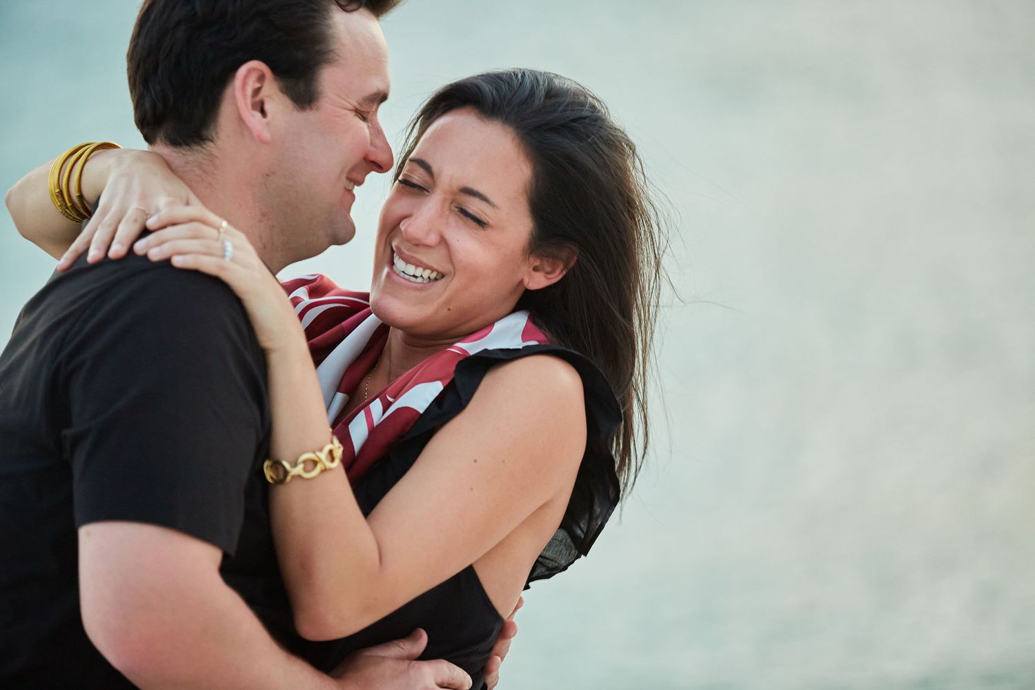 Happy woman smiling and hugging man closely during romantic beach engagement moment.