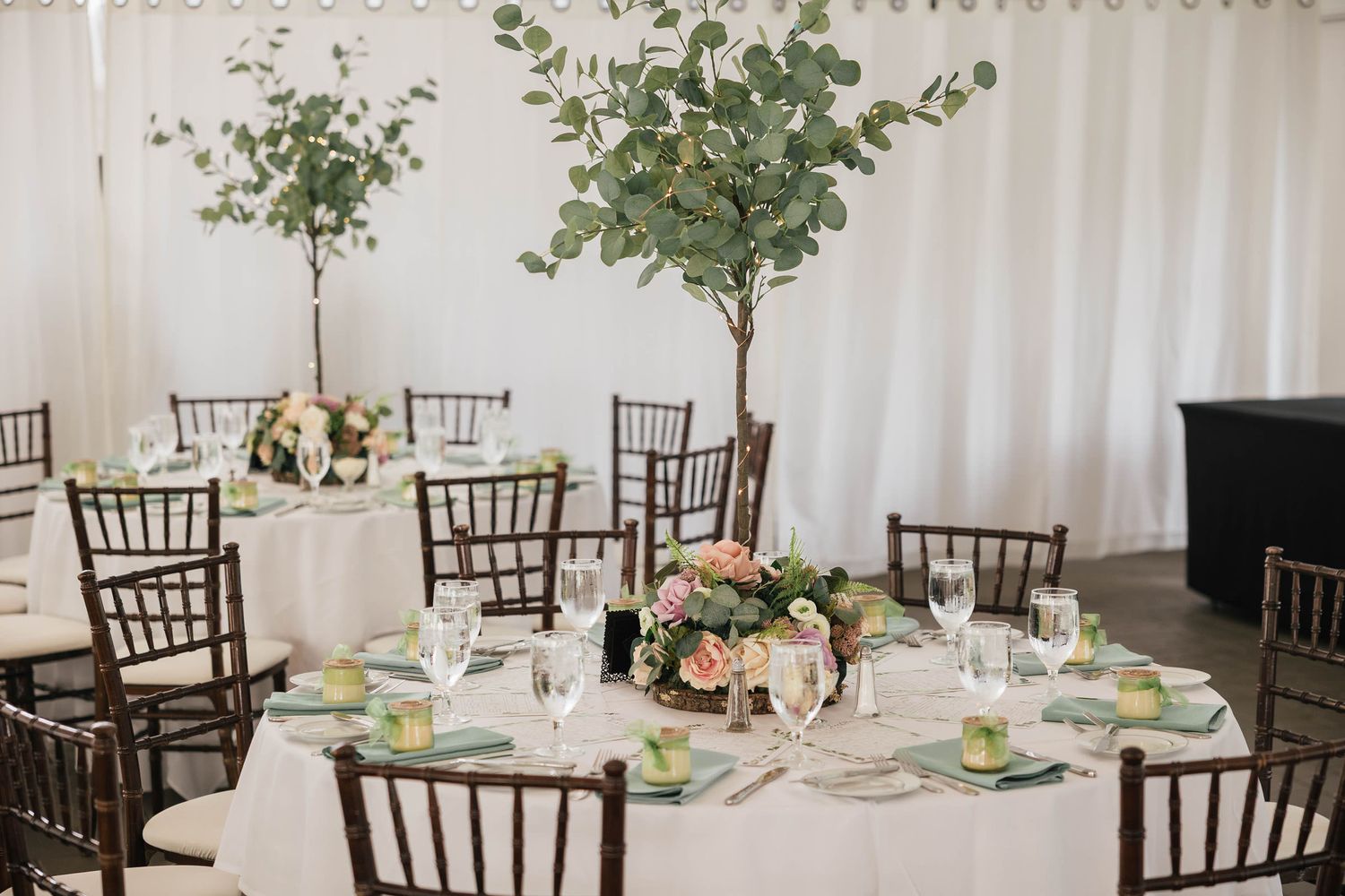 Reception tent set with round tables, sage green linens, floral centerpieces, and tall lit trees at Searles Castle in Windham, NH.