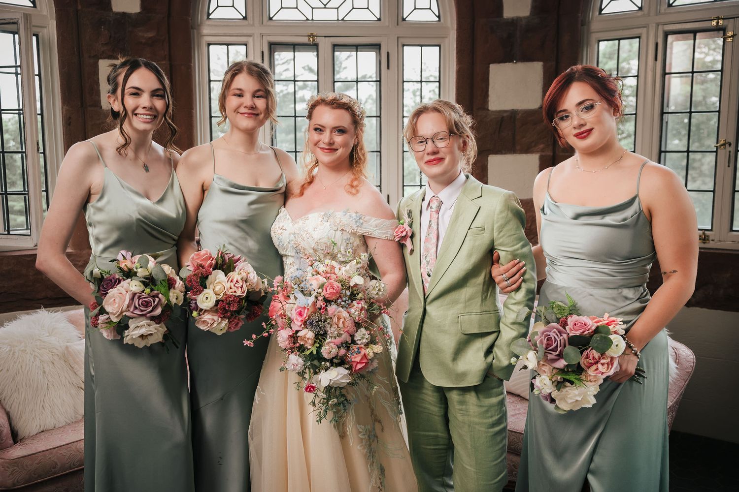 Bride and her bridesmaids smiling together, holding bouquets, in the sunroom at Searles Castle.