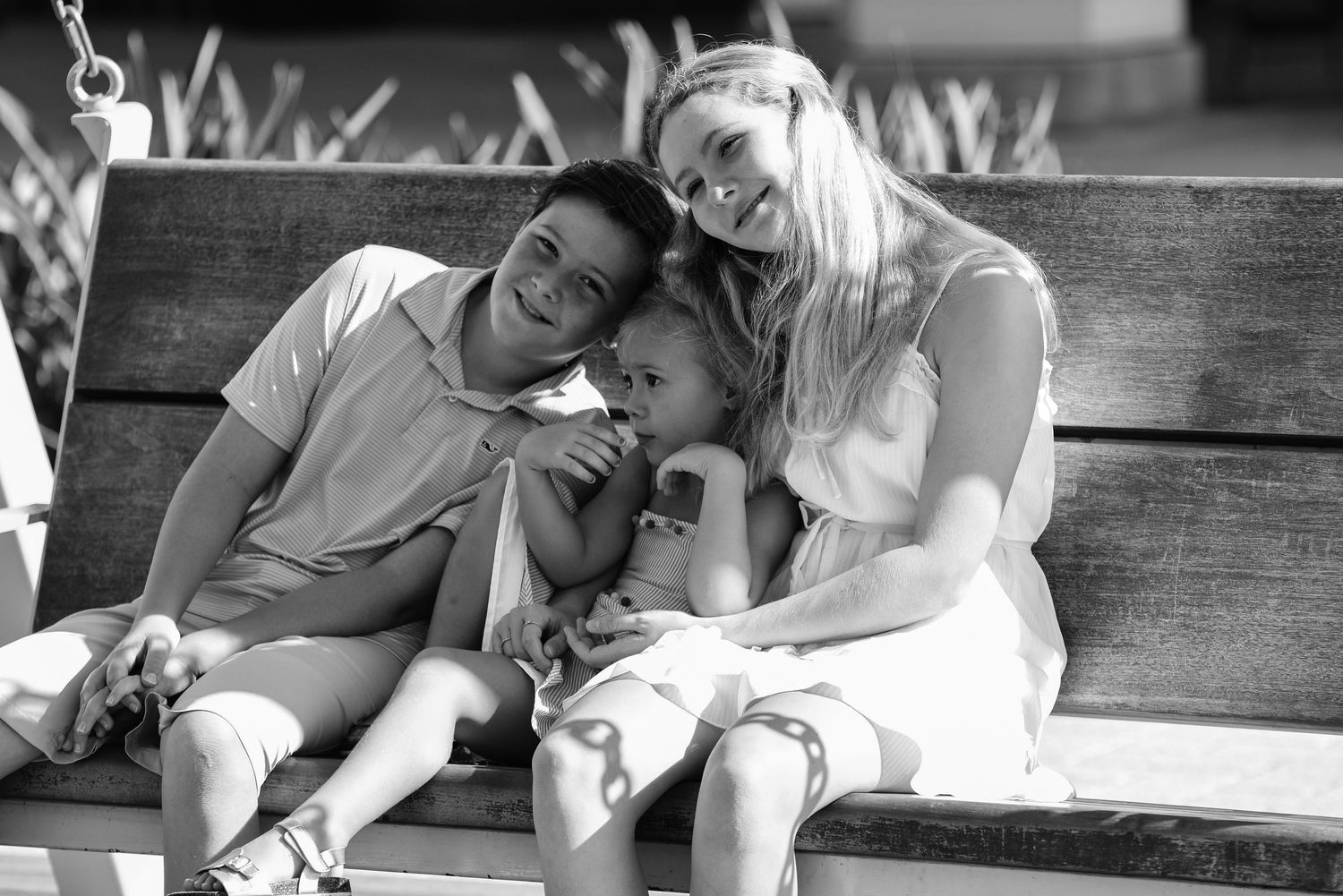 Black and white photo of a happy family with two parents and a young child sitting together on a wooden bench.