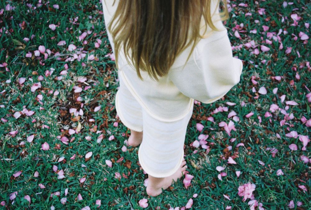 Person in white outfit standing barefoot on green grass scattered with pink flower petals.