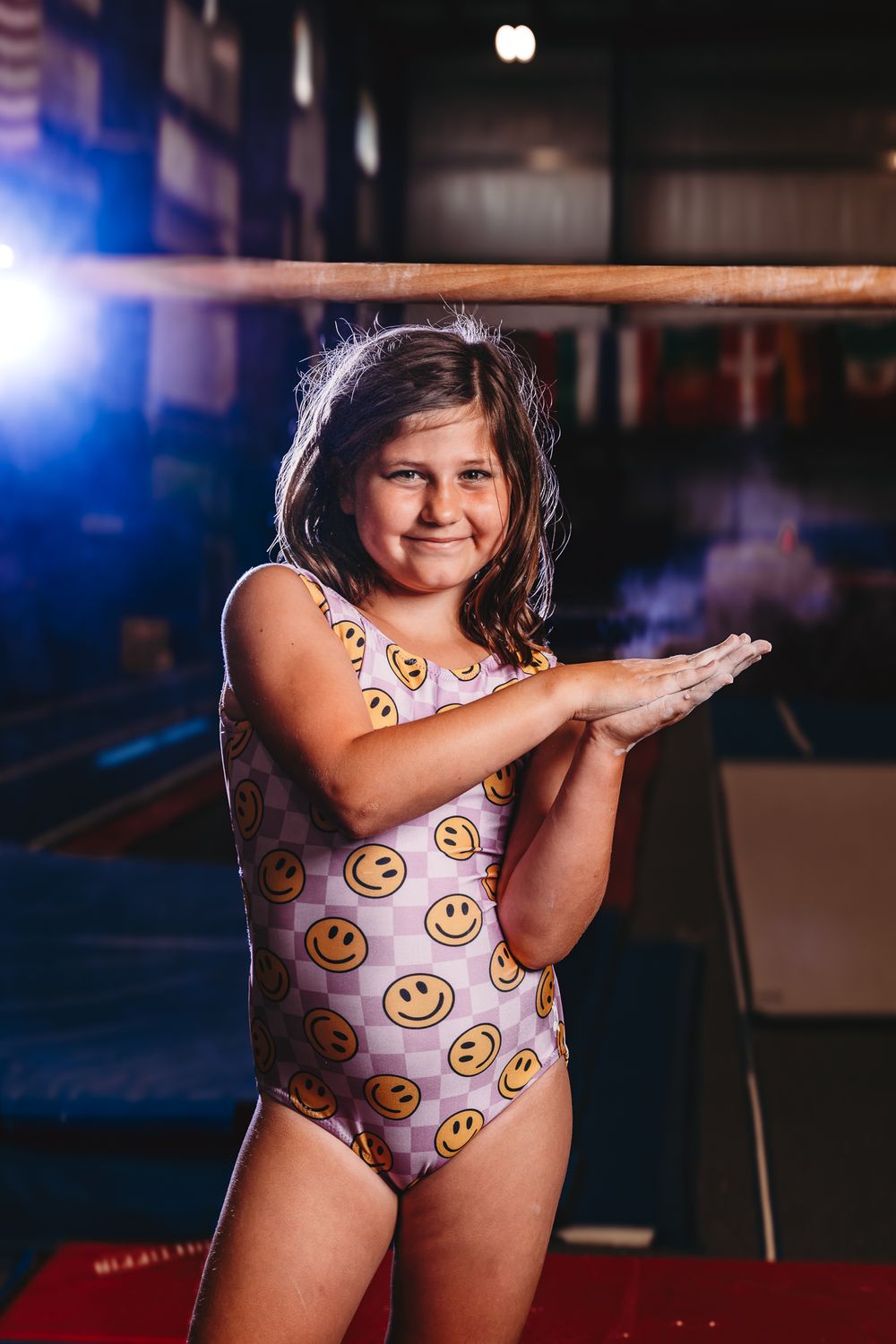 Young girl in smiley face swimsuit clapping hands at gymnastics gym.