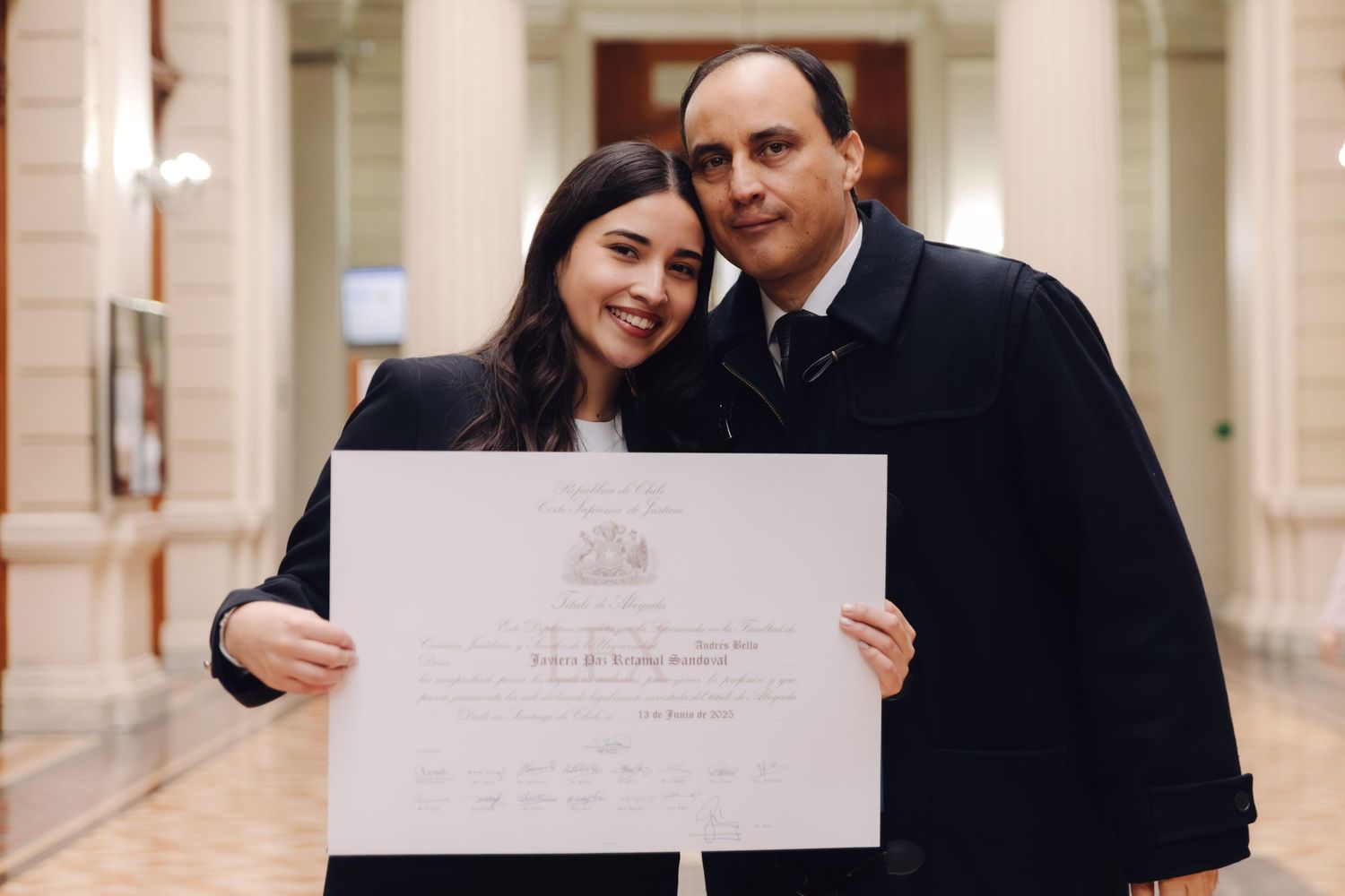 Woman and older man smiling together while proudly holding a graduation diploma certificate indoors.