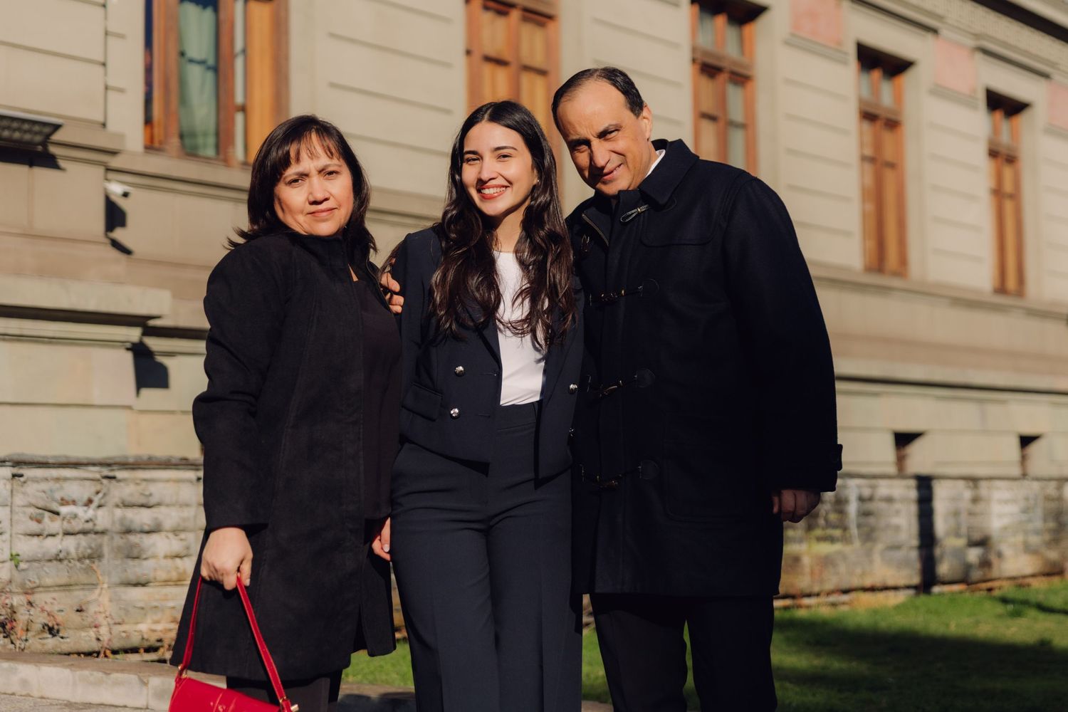 A young woman in a navy blazer posing with two older adults outside a historic building.