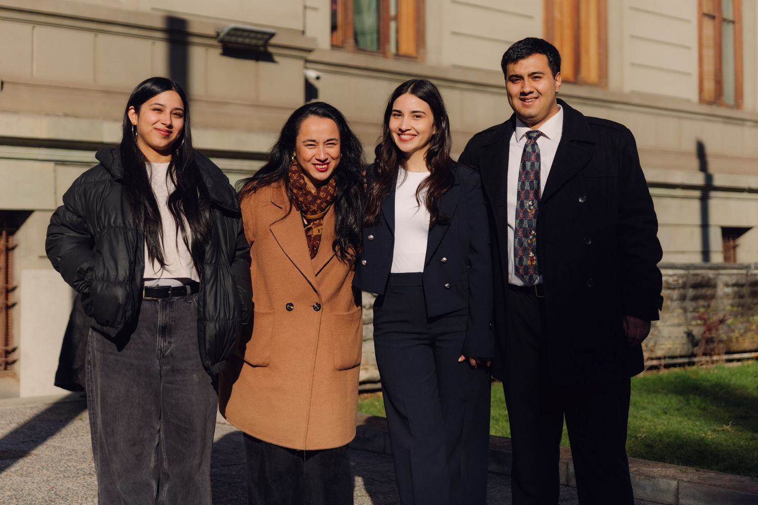 Four young professionals smiling together outside a classic building.