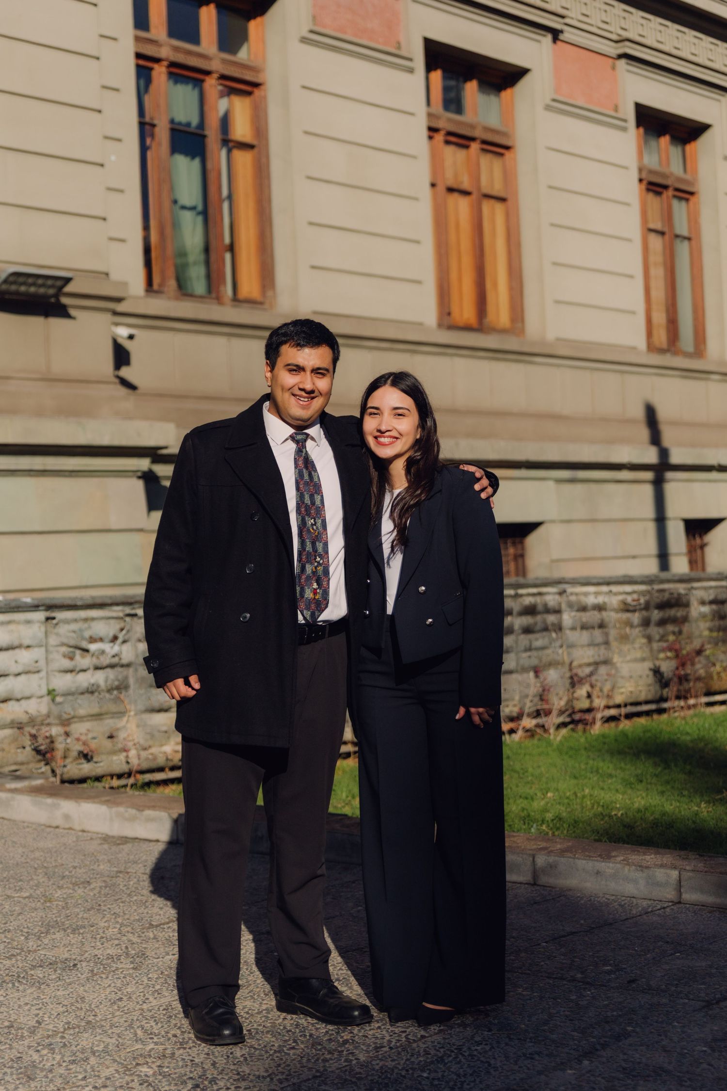 Young man and woman in formal attire posing together outside a historic building.